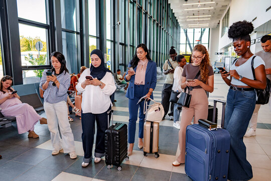 Diverse travelers using smartphones standing in airport terminal