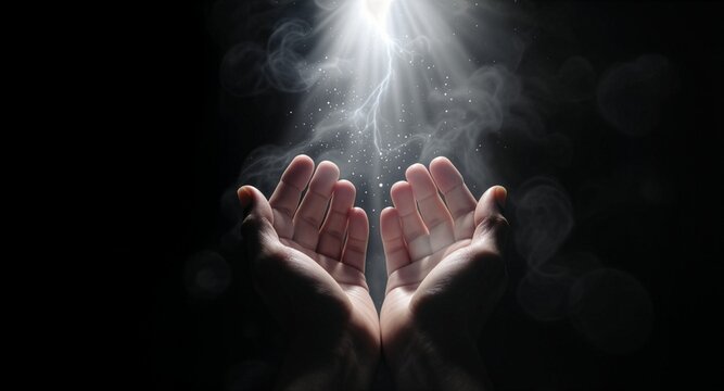 Two human hands opened in prayer, receiving a dramatic divine light with smoky etherial effects and glowing dust particles, isolated against a dark black background to imply faith.