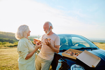 Fototapeta premium Senior couple sharing a meal by their compact car on a sunny day, representing retirement, travel, and adventure