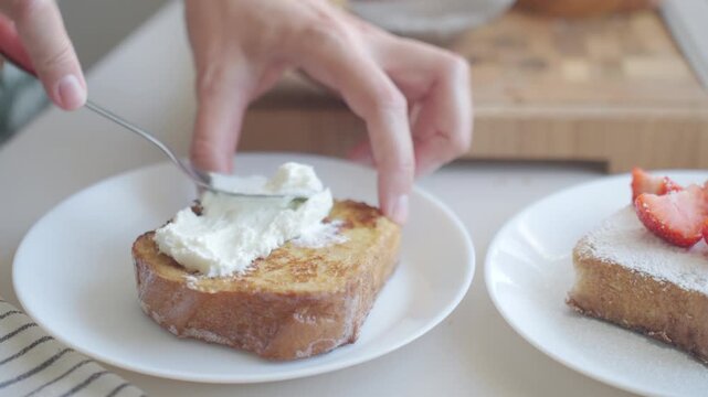 French toast topped with cream on a white plate, with another slice covered in powdered sugar and strawberries nearby. Concept of homemade breakfast and brunch