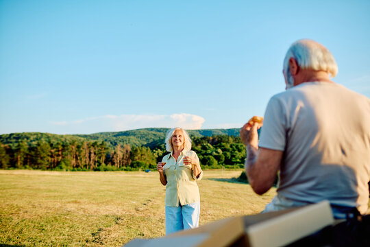 Senior couple sharing a happy moment, eating picnic snacks outdoors in a field, celebrating retirement together