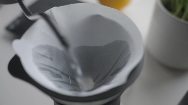 Water is poured into paper filter inside coffee dripper on glass carafe. Concept of pour over coffee and filter rinsing