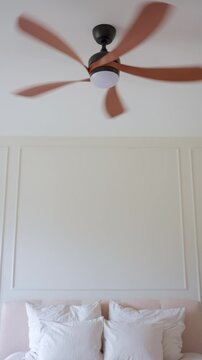 Ceiling fan begins rotating above bed in modern bedroom. Concept of home cooling and energy efficient climate control
