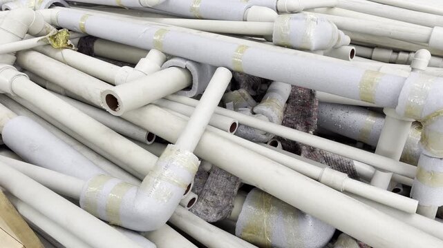 A pile of disassembled plastic water pipes with foam thermal insulation lies stacked outdoors. These plumbing materials are collected and prepared for waste management