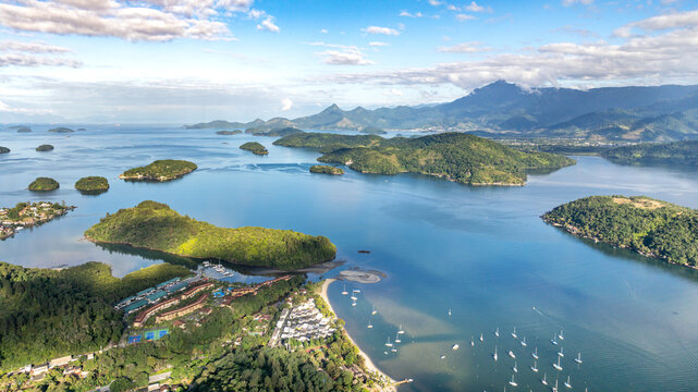 Aerial view of lush islands and coastal waters with sailboats anchored in the bay, dense green vegetation, and distant mountains in Angra dos Reis, Rio de Janeiro, Brazil.