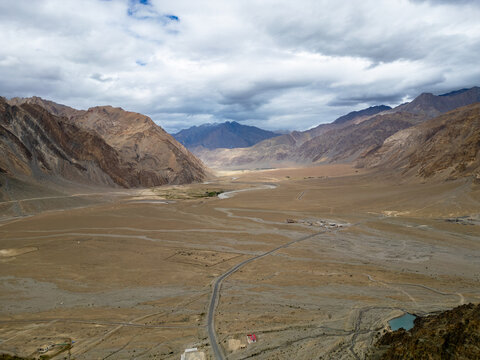 Aerial view of the Zanskar Valley featuring a winding river, arid mountain landscape, and a road stretching through the vast desert terrain in Zanskar, Ladakh, India.