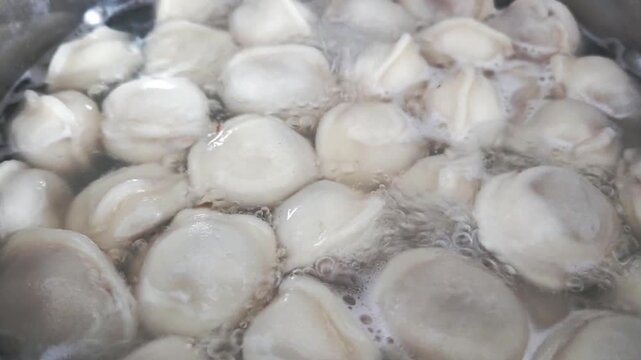 Boiling dumplings in a pot filled with water, showcasing the gradual cooking process as they float and bubble in the hot liquid