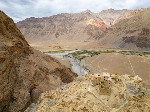 Aerial view of Zanskar monastery perched on a rocky cliff overlooking the winding river and vast arid mountain landscape in Zanskar, Ladakh, India.