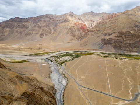 Aerial view of the rugged Zanskar valley landscape featuring a winding river, a small bridge, and a road cutting through the arid, rocky terrain in Zanskar, Ladakh, India.