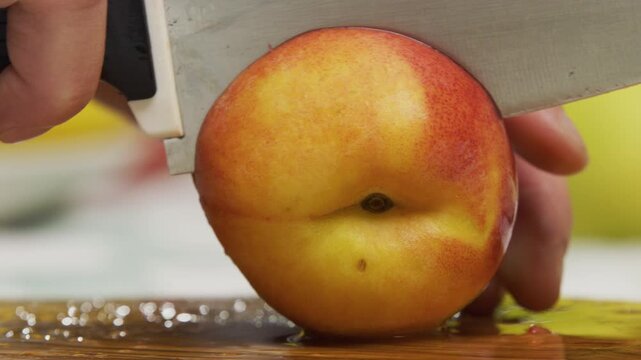 Large knife slicing through fresh peach on chopping board - slow motion