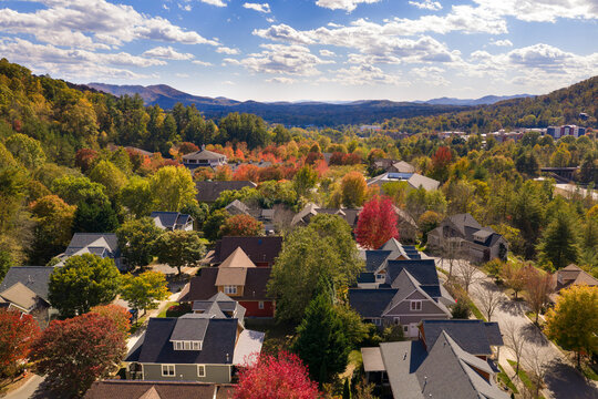 Scenic mountain community with private homes surrounded by dense woodland glowing with vibrant autumn colors. Aerial view of peaceful countryside living.
