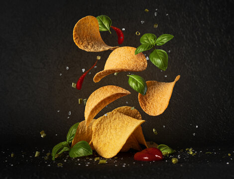 Crispy potato chips in motion with fresh basil and ketchup on black background