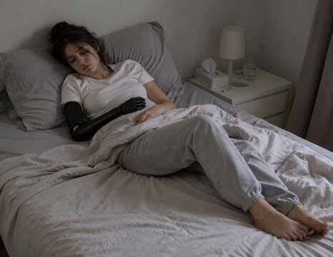 Young woman with prosthetic arm resting in bed while feeling unwell