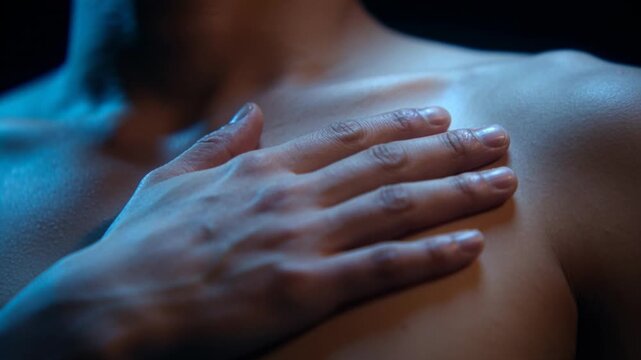 Moving right hand, bare-chested man placing palm over left pectoral in studio, cool blue rim light