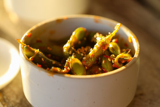 Close‑up of spicy edamame sprinkled with sesame seeds and chili flakes in warm sunlight, highlighting texture and vibrant flavor.
