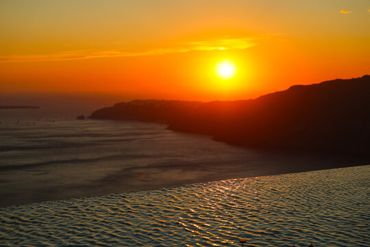 Golden sunset over the Aegean Sea viewed from an infinity pool in Santorini, Greece, reflecting warm light and tranquil coastal beauty.