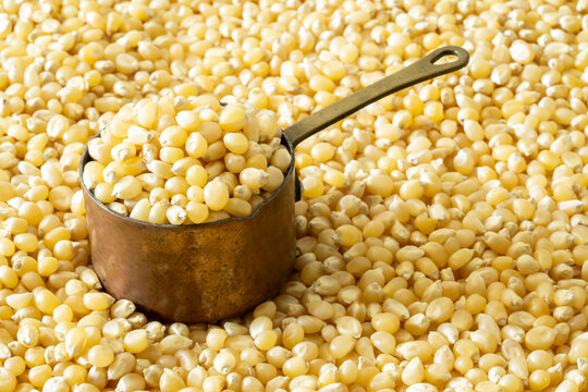 Closeup of un-popped kernels of popcorn with a copper measuring cup