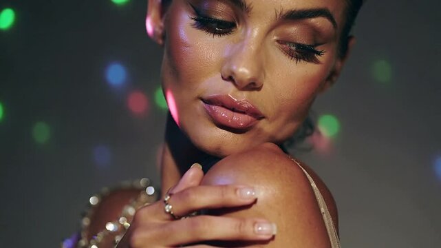 Posing sequin-strap model lifting hand on shoulder in studio, disco lights hitting bracelets, ring