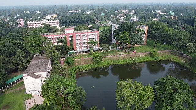 Aerial view of a campus with buildings and a large pond an overhead perspective shows institutional surrounded by lush green trees near pond, illustrating calm educational