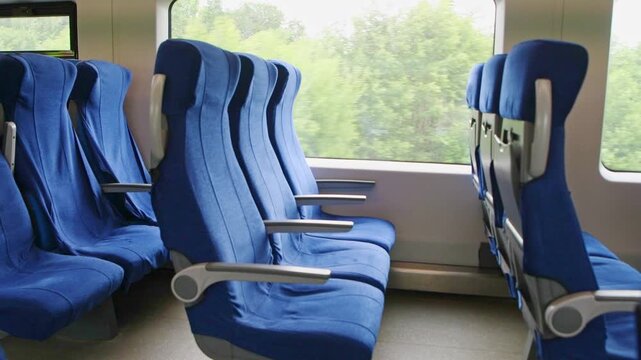 Blue fabric seats inside moving train carriage with green landscape through large windows