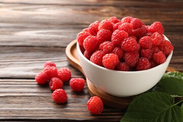 Tasty ripe raspberries in bowl and leaves on wooden table, closeup. Space for text © New Africa