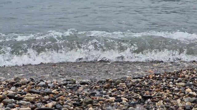Sea water waves gently rolling onto a tranquil shoreline with colorful smooth stones