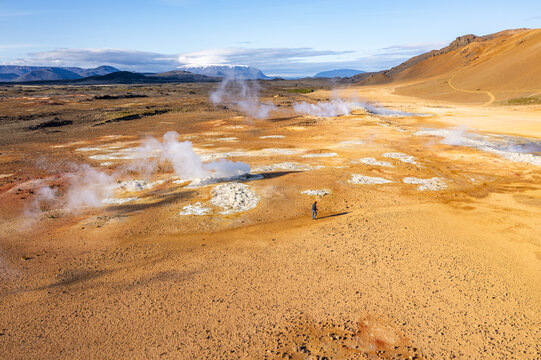 Aerial view of Hverir geothermal field with steaming fumaroles, bubbling mud pots, and a lone person walking across the orange volcanic landscape, Reykjahlid, Thingeyjarsveit, Iceland.