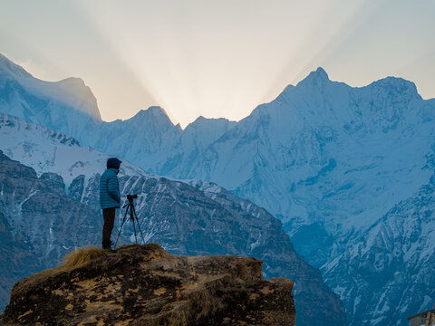 Aerial view of a photographer with a camera on a tripod standing on a rocky outcrop overlooking the snow-capped Himalayan mountains at sunrise in Nepal.