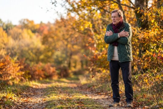 Senior man standing cold and shivering outdoors in an autumn forest landscape