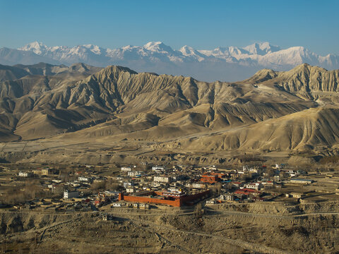 Aerial view of the historic Kag Chode Thupten Samphel Ling Monastery with red walls in Kagbeni, surrounded by the arid landscape of the Mustang region and Himalayan peaks in Nepal.