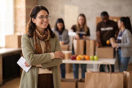 Woman standing arms crossed, smiling while looking away, with other volunteers working in background