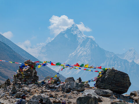 Aerial view of the majestic Ama Dablam mountain peak in the Himalayas, featuring colorful prayer flags fluttering in the wind over a rugged rocky landscape in Nepal.