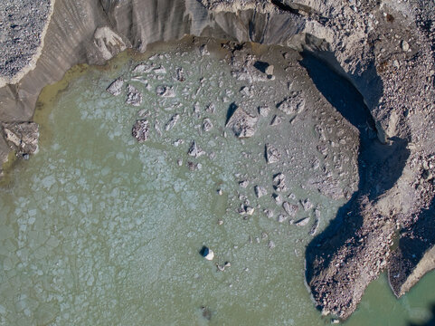 Aerial view of a glacial lake with floating ice chunks and meltwater surrounded by rocky moraine terrain in Nepal.