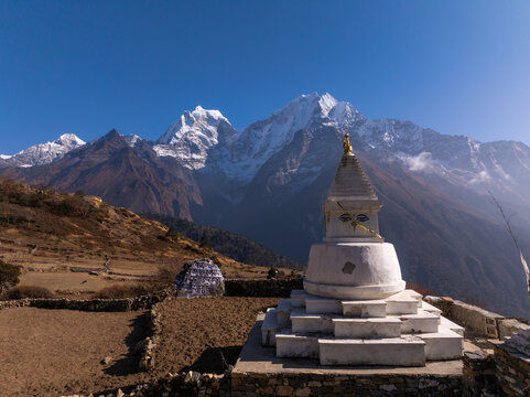 Aerial view of a white Buddhist stupa with prayer flags set against the backdrop of snow-capped Himalayan mountains in Nepal.