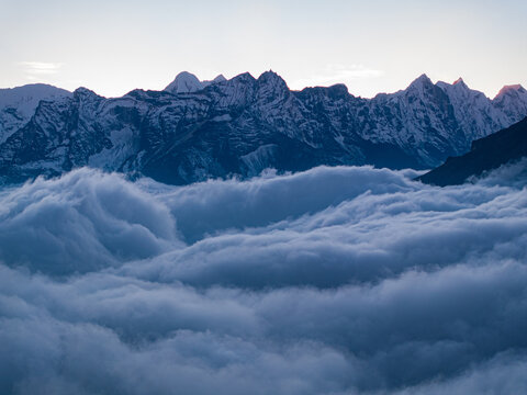 Aerial view of the snow-capped Himalayan mountain range rising above a dense sea of clouds at dawn in Nepal.