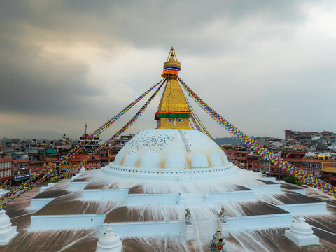Aerial view of the Boudhanath Stupa with its iconic golden spire and colorful prayer flags surrounded by the urban landscape of Kathmandu, Nepal.