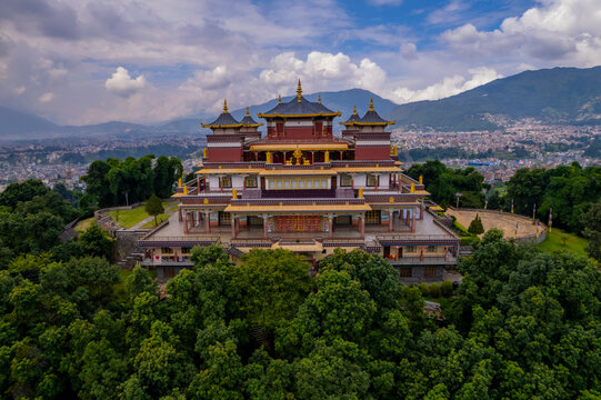 Aerial view of Kopan Monastery surrounded by lush green trees with the Kathmandu Valley in the background under a cloudy sky in Nepal.
