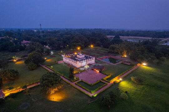 Aerial view of the Maya Devi Temple in Lumbini illuminated at dusk, surrounded by lush gardens and pathways in Nepal.