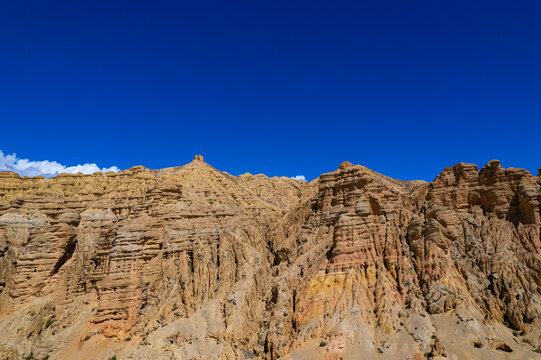 Aerial view of arid, layered rock formations and steep mountain cliffs under a clear blue sky in Nepal.