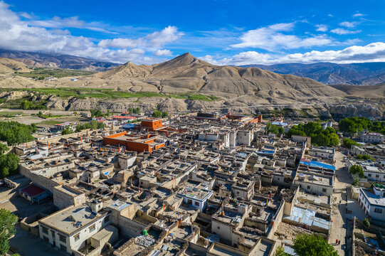 Aerial view of the historic town of Lo Manthang with traditional stone houses, a prominent red monastery, and prayer flags set against the arid mountain landscape of Nepal.