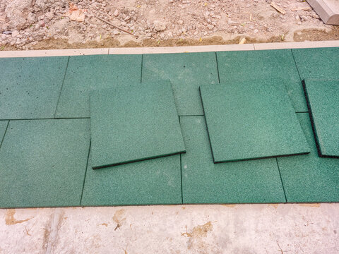 Green rubber playground tiles being installed on a concrete surface