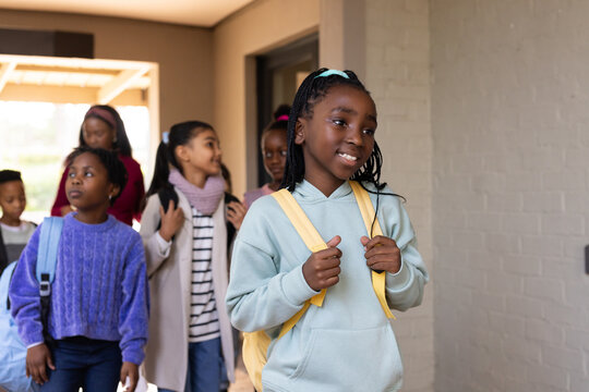 African American teen girls walking in school entry smiling with yellow-blue backpacks, copy space