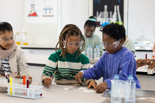 African American teen students conducting lab experiment at school with petri dishes and goggles