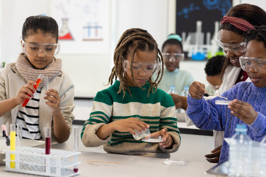 African teenage students and teacher in labcoat conducting experiment at bench petri dish goggles