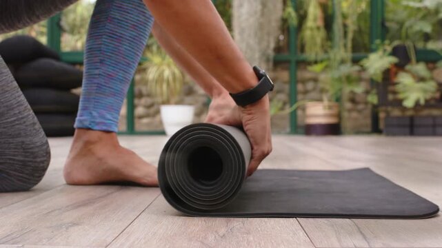 Woman reaching forward and pulling rolled black yoga mat, unrolling and smoothing for yoga practice