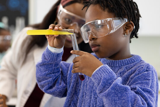 African female teacher guiding child holding test tube with purple liquid using yellow pipet in lab