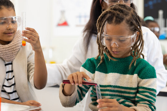 African American students with teacher working at school lab pipetting into test tube with goggles
