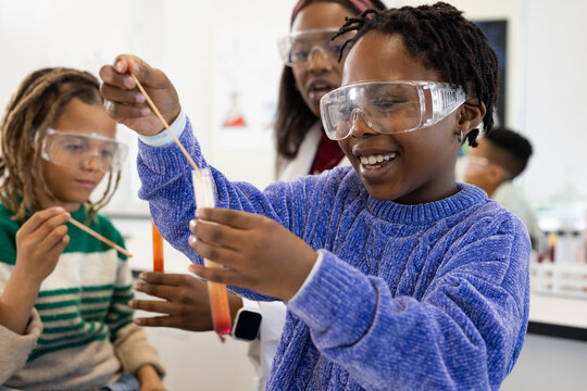 African American teacher with students guiding experiment at school, child holding orange test tube