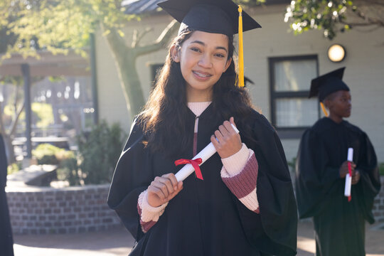 African American youth graduates smiling, holding diplomas with red ribbons in campus courtyard