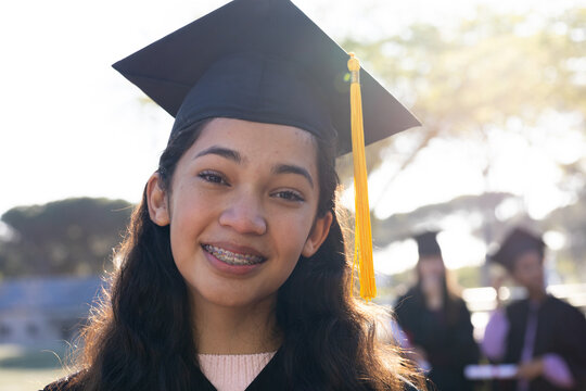 African American youth grad smiling and wearing black cap with yellow tassel and gown on campus